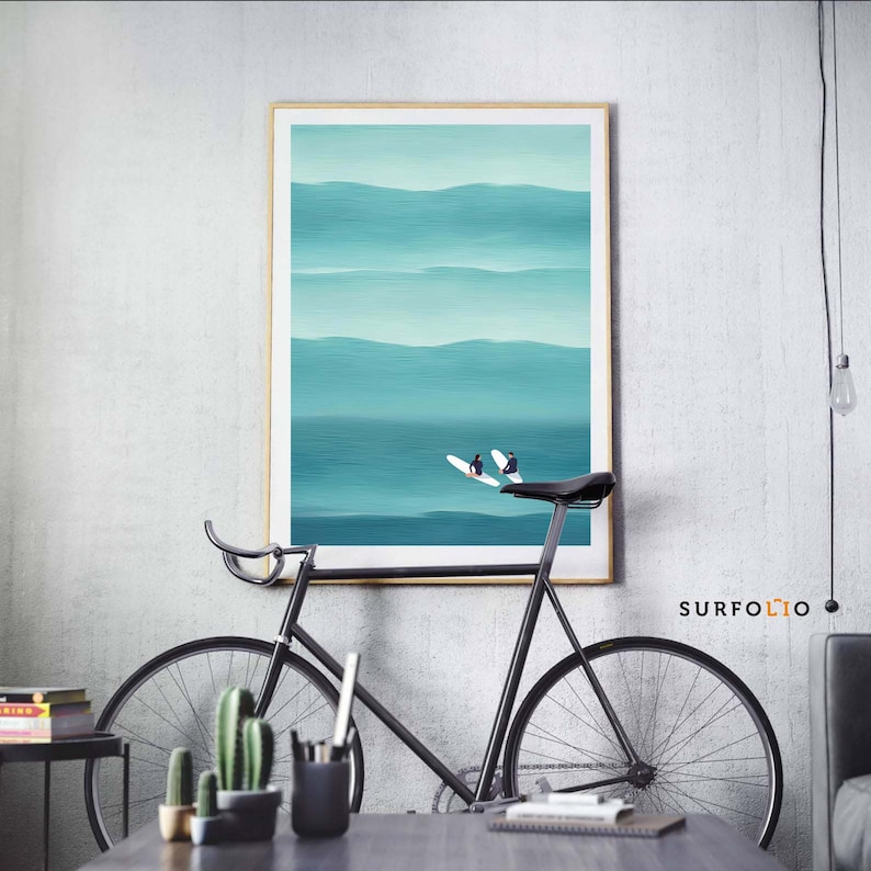 May include: A framed abstract painting of a turquoise ocean with two surfers riding waves. The painting is hanging on a white wall above a black bicycle.