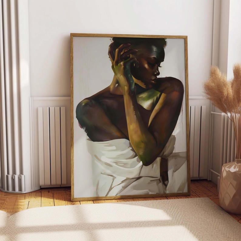 May include: A framed art print featuring a portrait of a person with dark skin, draped in white fabric. The artwork has a warm color palette with green and brown tones. The frame is made of light-colored wood.