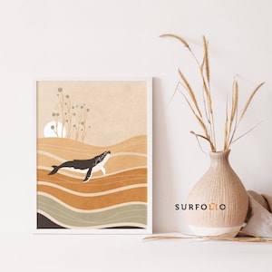 May include: A framed art print featuring a whale swimming in the ocean. The artwork has a minimalist style with a color palette of brown, beige, and white. The print is displayed on a white surface, with a vase of dried plants to the right.