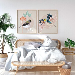 May include: Two framed prints of stylized birds with floral designs. The prints are hanging on a white wall above a bed with a white duvet and a wooden headboard.