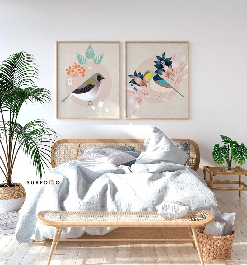 May include: Two framed prints of stylized birds with floral designs. The prints are hanging on a white wall above a bed with a white duvet and a wooden headboard.