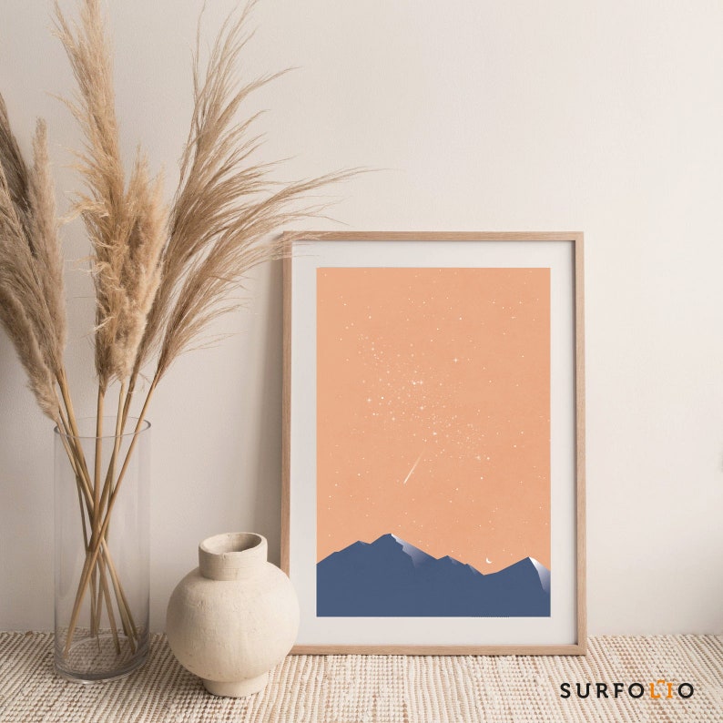 Pode incluir: Uma impress&atilde;o emoldurada com um fundo p&ecirc;ssego e uma silhueta de montanhas em azul. A impress&atilde;o apresenta uma estrela cadente branca e pontos brancos que representam estrelas.
