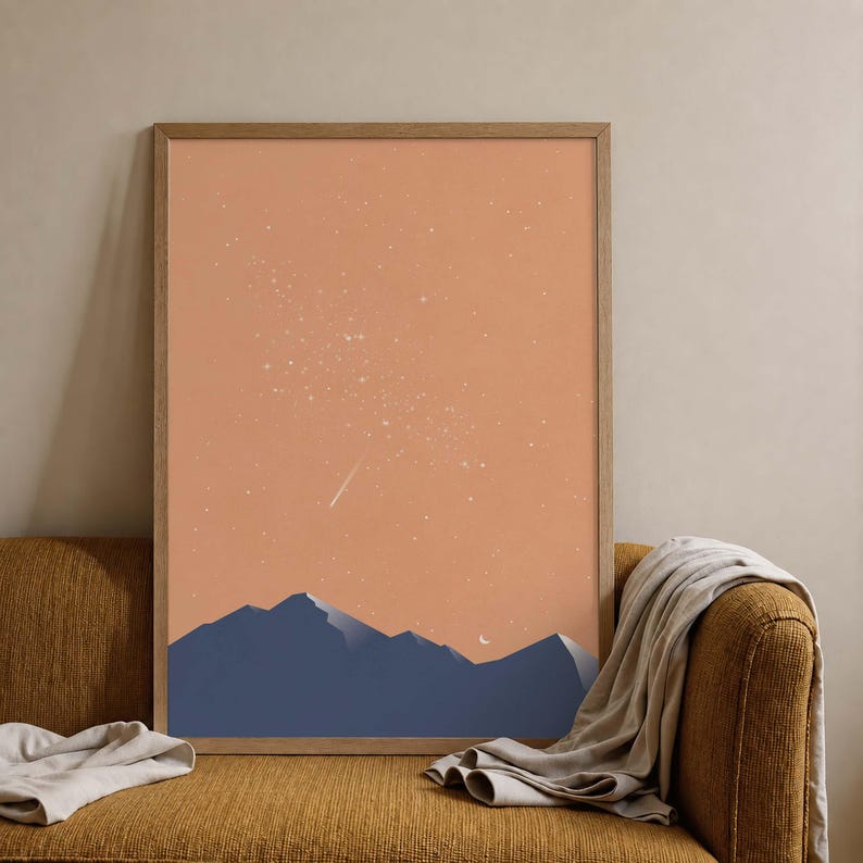 May include: A rectangular wall art print in a wooden frame featuring a dark blue mountain range silhouette against a solid peach-colored sky. The sky is filled with small white stars and a single shooting star, with a small white crescent moon.