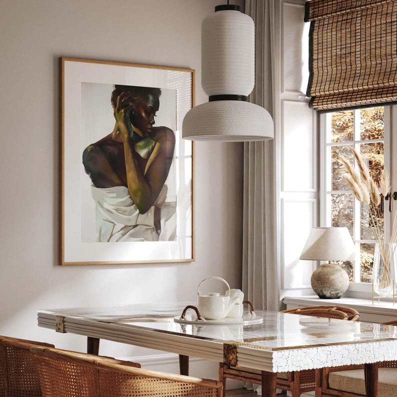 May include: A dining room scene featuring a framed artwork of a person, a white pendant light, and a table set with a teapot and cups. The room has a neutral color palette with natural light from a window with a woven shade.