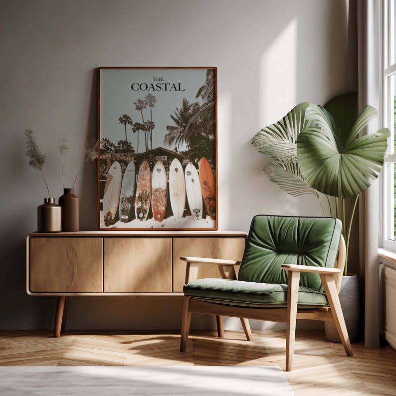 May include: A framed print titled "The Coastal" featuring surfboards lined up on a beach with palm trees. The print hangs above a wooden cabinet with vases. A green armchair sits nearby.