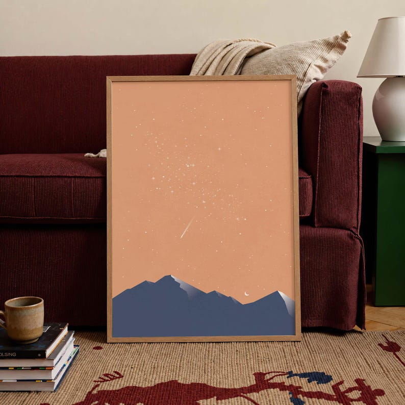 May include: A framed wall art print featuring a minimalist landscape illustration. The artwork displays dark blue mountain silhouettes against a solid peach-colored sky filled with scattered white stars, a small crescent moon, and a single shooting star.