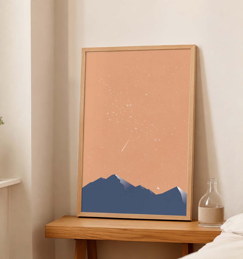 May include: A vertical rectangular framed wall art print featuring a dark blue mountain range silhouette against a solid peach-colored sky. The sky is filled with scattered white stars and a single shooting star, with a small white crescent moon.