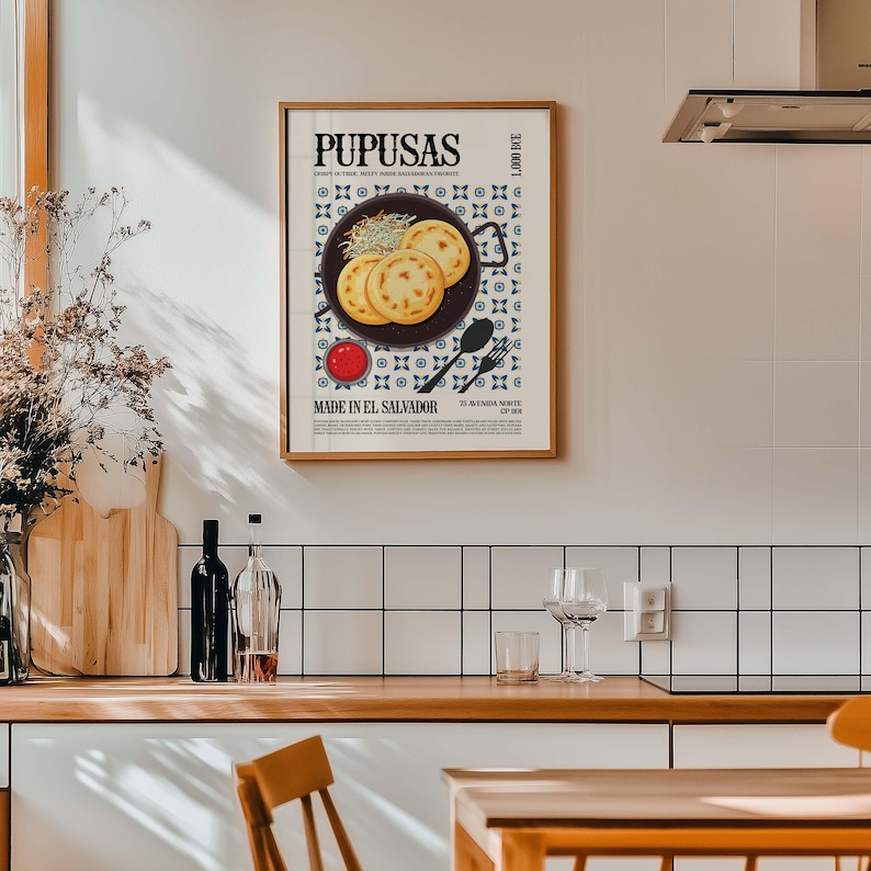 May include: A framed poster with the word "PUPUSAS" in bold letters. The poster features an illustration of pupusas, a traditional Salvadoran dish, on a plate with a side of sauce. The text "MADE IN EL SALVADOR" is also visible.