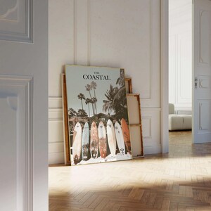 May include: A framed print titled "The Coastal" featuring a beach scene with palm trees and a row of surfboards. The surfboards are various colors and designs, leaning against a sandy area.