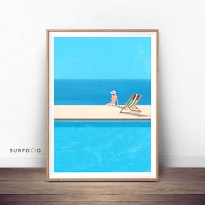 May include: A woman in a white hat sits on a lounge chair by a swimming pool. The pool is surrounded by a white sand beach and the ocean is in the background. The sky is blue.