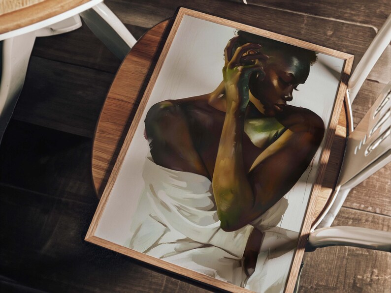 May include: A framed art print featuring a portrait of a person with dark skin, draped in white fabric. The artwork has a warm color palette with shades of brown, green, and white. The frame is made of light-colored wood, and the print is resting on a wooden surface.