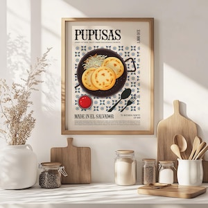 May include: A framed poster featuring a culinary illustration of pupusas, a Salvadoran dish. The poster includes the text "PUPUSAS" and "MADE IN EL SALVADOR". The image shows three pupusas on a plate, with a side of sauce and a decorative pattern.