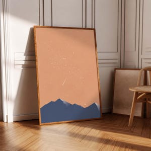 May include: A rectangular framed wall art print featuring a dark blue mountain range silhouette against a solid peach-colored sky filled with white stars and a small crescent moon. The artwork is encased in a simple, thin wooden frame.
