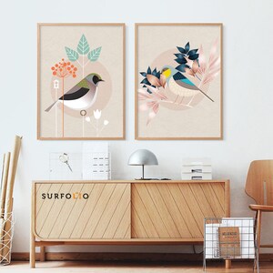 May include: Two framed prints with a minimalist design featuring stylized birds and floral elements. The prints have a light beige background with pink, blue, and green accents. The prints are displayed on a wooden shelf with a lamp and other decorative items.