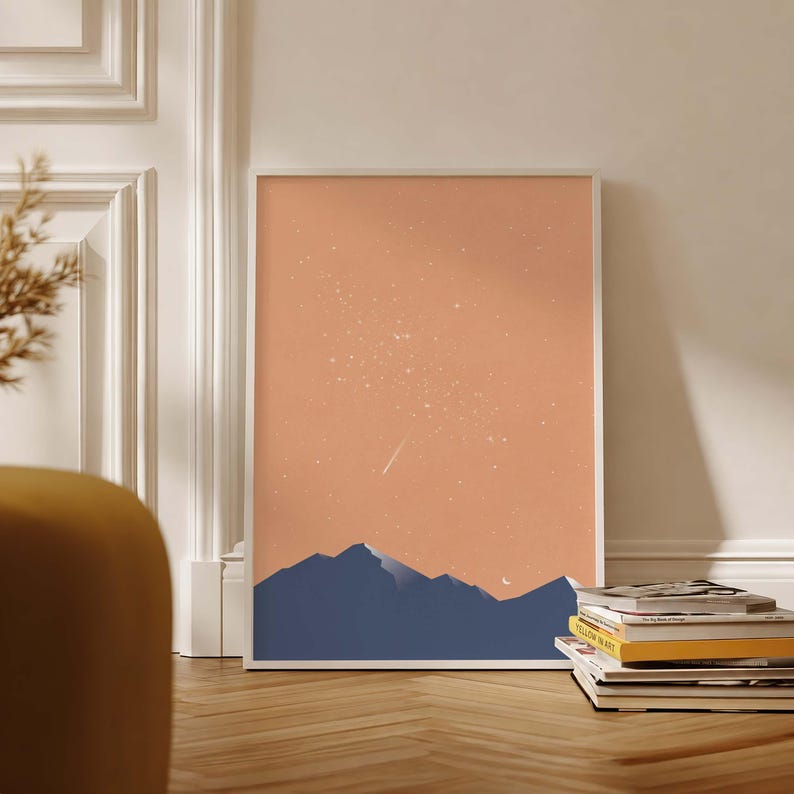 May include: A rectangular wall art print featuring a dark blue mountain range silhouette against a solid peach-colored sky. The sky is filled with a scattering of small white stars and a single diagonal shooting star streak in the upper center.