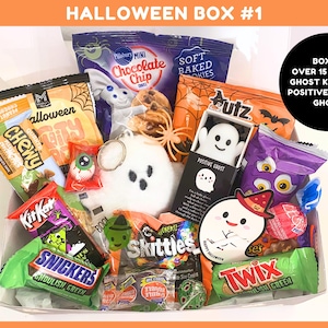 May include: A Halloween gift box containing over 15 treats, including a plush ghost keychain, a positive squishy ghost, and various snacks like Pillsbury cookies, Utz chips, Skittles, KitKat, Snickers, and Twix bars with Halloween-themed packaging.