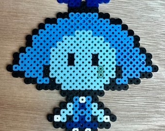Puede incluir: Un personaje de pixel art azul con una cabeza redonda, dos brazos pequeños y dos piernas. El personaje lleva un vestido azul y blanco y un lazo azul en la cabeza.