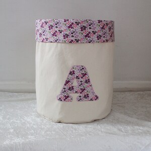 May include: A white canvas storage bin with a purple and pink floral print fabric top and a large purple and pink floral print letter A on the front.