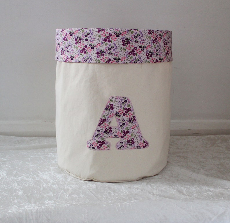 May include: A white canvas storage bin with a purple and pink floral print fabric top and a large purple and pink floral print letter A on the front.