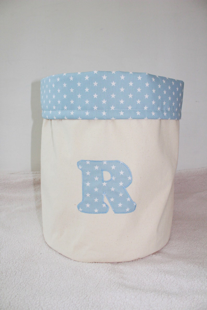 May include: A white canvas storage bin with a blue star patterned fabric top and a blue star patterned letter "R" on the front.