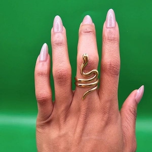 May include: A gold-toned metal ring shaped like a coiled snake that wraps around the finger. The snake design features a smooth, polished surface with a defined head at the top and a tapering tail at the bottom, creating a continuous spiral band.