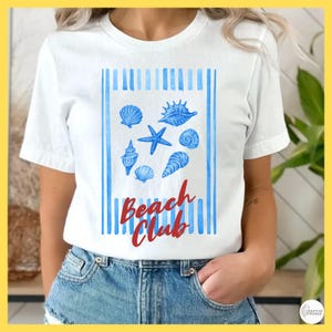 May include: A white short-sleeve t-shirt featuring a central rectangular graphic with vertical blue stripes. The design includes various blue seashells and a starfish, with the red cursive text Beach Club printed below the sea life illustrations.