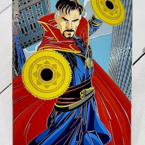 May include: A colourful illustration of Doctor Strange, a superhero from Marvel Comics, wearing a red cape and blue robe. He is holding two golden discs with a black star in the centre. The background is a cityscape.
