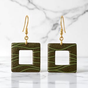 May include: A pair of square earrings with a gold-colored hook. The earrings are olive green with a lighter green wavy pattern. The center of each earring is a square cutout.