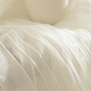 May include: White sheer curtain fabric with a textured, woven pattern. The fabric has a subtle sheen and a delicate, airy feel.