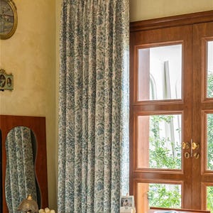 May include: A pair of white curtains with a blue floral pattern hang in a window. The curtains are made of a lightweight fabric and have a subtle sheen. The window is framed by a wooden door with a glass panel.