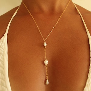 May include: A delicate gold-colored necklace featuring three white, teardrop-shaped pearls. The necklace has a Y-shaped design, with the pearls suspended from a fine chain. The necklace is a piece of jewelry.