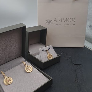 May include: Three green jewelry boxes with gold pomegranate earrings and a gold pendant necklace. The boxes are on a black surface. The pendant necklace is in a smaller box. The earrings are in a larger box. The boxes have a white label with the text "ARIMOR Jewelry - Since 1989".
