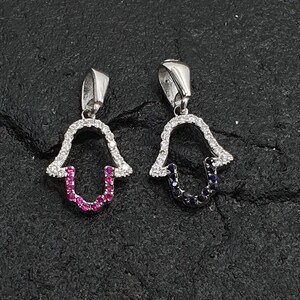 May include: Two silver Hamsa hand charms with cubic zirconia stones. One charm has pink stones in the center and the other has blue stones.