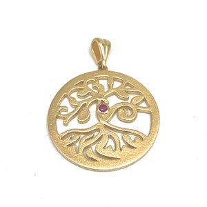 Pode incluir: Pingente dourado com um design de árvore da vida com uma pequena gema vermelha no centro. O pingente é circular e tem um design delicado e intrincado.