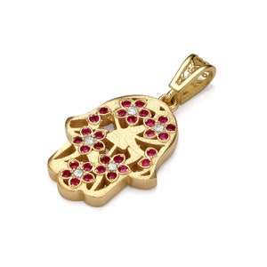May include: Gold pendant charm in the shape of a hamsa hand with a filigree design and red and white gemstones.