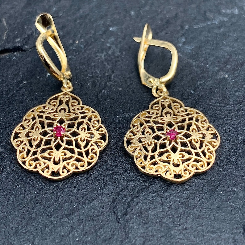 May include: A pair of gold filigree earrings with a red gemstone in the center of each earring.