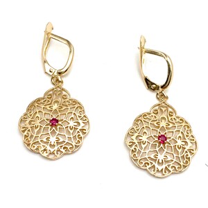 May include: A pair of gold filigree earrings with a red gemstone in the center of each earring.