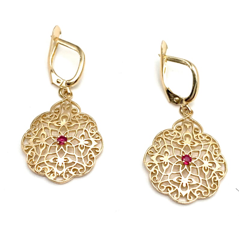 May include: A pair of gold filigree earrings with a red gemstone in the center of each earring.