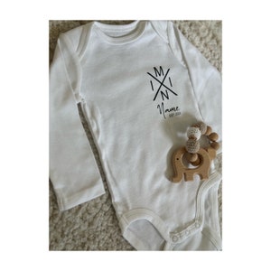Könnte beinhalten: Weißer Langarm-Babybody mit einer schwarzen Grafik eines Kreuzes mit den Buchstaben "M I N I" und dem Text "Name Est 2024".