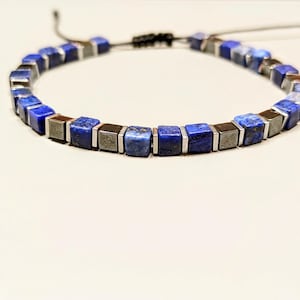 Può includere: Un braccialetto con perline quadrate blu e argento. Il braccialetto presenta perline quadrate blu scuro e argento alternate, infilate su un cordino nero. Il braccialetto è regolabile.