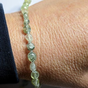 May include: A green and black gemstone bracelet with a beaded design. The bracelet is made of small, round beads that are strung together on a clear elastic cord.