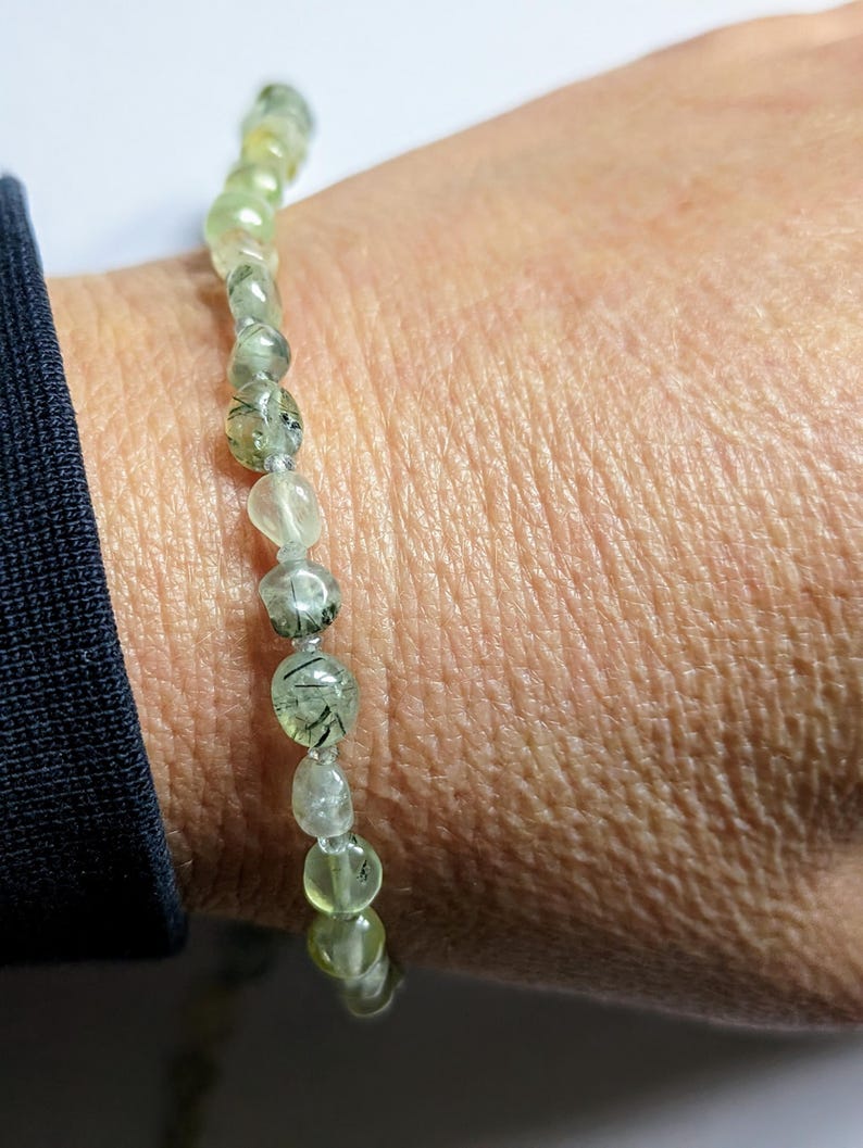 May include: A green and black gemstone bracelet with a beaded design. The bracelet is made of small, round beads that are strung together on a clear elastic cord.