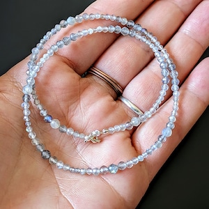 May include: A delicate necklace made with small, iridescent labradorite beads. The necklace is approximately 18 inches long and features a simple silver clasp.