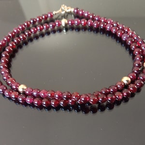 May include: A double strand necklace made of dark red gemstone beads with gold accents.