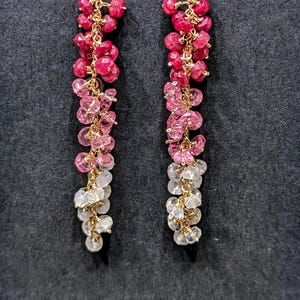 Puede incluir: Un par de pendientes largos y colgantes con un degradado de piedras preciosas rojas, rosas y blancas. Los pendientes están hechos de oro y presentan un racimo de pequeñas piedras preciosas redondas.