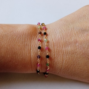 May include: A gold chain bracelet with multi-colored beads. The beads are pink, green, and black.