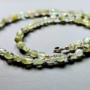 May include: A green and white gemstone necklace with a silver clasp. The necklace is made of oval-shaped beads.