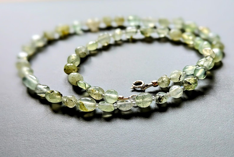 May include: A green and white gemstone necklace with a silver clasp. The necklace is made of oval-shaped beads.