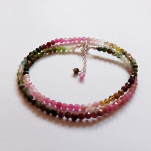 May include: A multi-colored gemstone bracelet with a silver clasp. The bracelet features a gradient of pink, green, and brown gemstones.