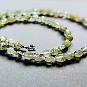 May include: A green and white gemstone necklace with a silver clasp. The necklace is made of oval-shaped beads.